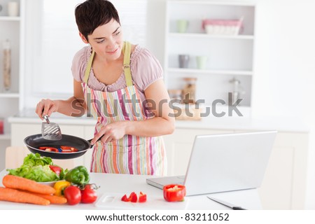 Beautiful woman cooking with receipt on laptop in the kitchen