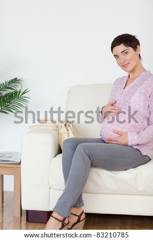 Pretty pregnant woman sitting on a sofa touching her belly in a waiting room
