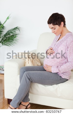 Brunette short-haired pregnant woman sitting on a sofa touching her belly in a waiting room