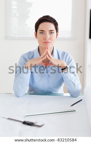 Thoughtful Woman with an architectural plan looking into the camera in an office