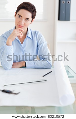 Thoughtful brunette Woman with an architectural plan looking into the camera in an office