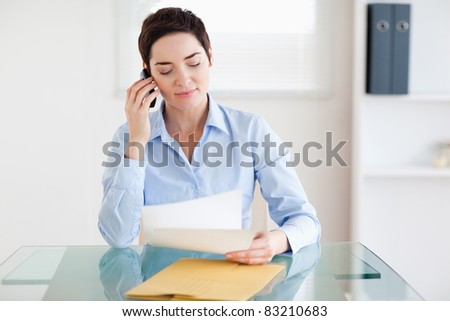 Portrait of a brunette Businesswoman sitting behind a desk with papers on the phone in an office