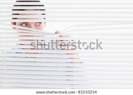 Curious businesswoman peeking out of a window in an office