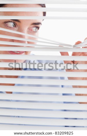 Beautiful businesswoman peeking through a venetian blind in an office