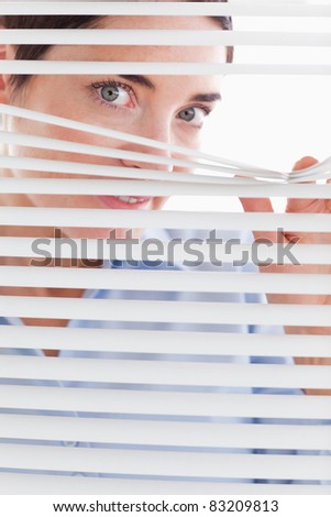 Beautiful brunette businesswoman peeking through a venetian blind in an office