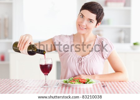 Woman pouring red wine in a glass in a kitchen
