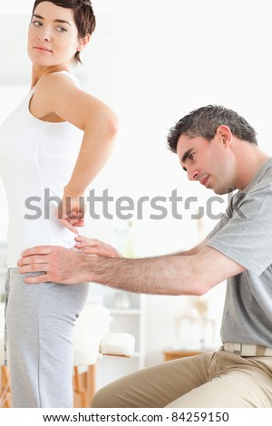 Chiropractor examining a brunette woman\'s back in a room