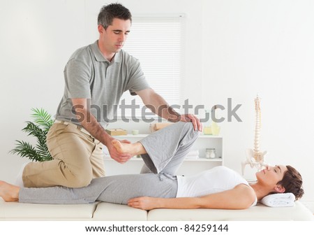 A chiropractor is stretching a young woman\'s leg