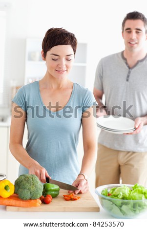Woman cutting vegetables and man holding plates in a kitchen