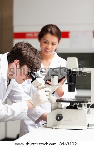 Portrait of a science student looking in a microscope while his classmate is writing in a laboratory