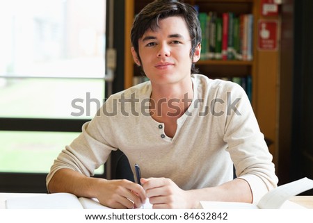 Smiling male student writing an essay in a library