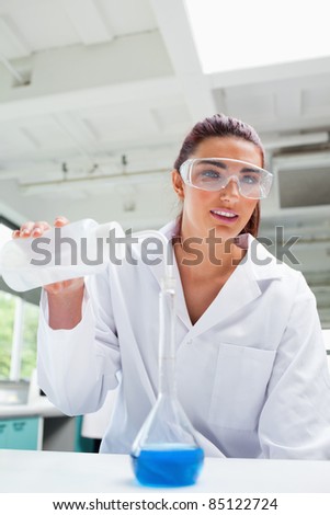 Portrait of a female science student pouring liquid with protective glasses while looking at the camera