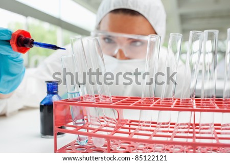stock photo : Protected female scientist dropping blue liquid in a test tube in a laboratory