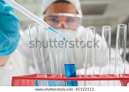 Protected science student dropping blue liquid in a test tube in a laboratory