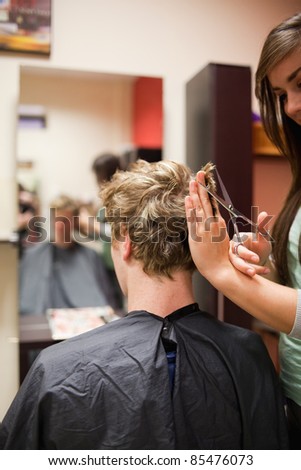 Portrait of a blond-haired man having a haircut with scissors