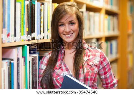 Smiling female student holding a book in a library