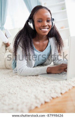 Close up of smiling woman lying on floor with her notebook listening to music