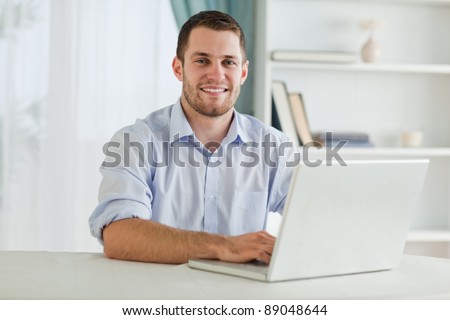 Smiling businessman with rolled up sleeves on his laptop in his home office