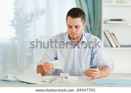 Young businessman with pocket calculator checking invoices