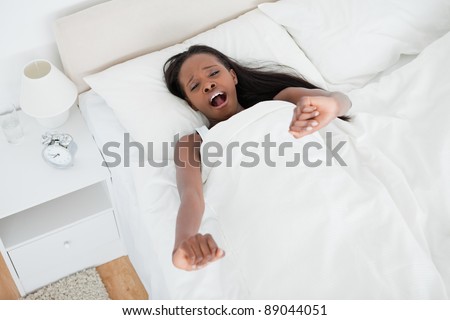 Tired woman stretching her arms and yawning in her bedroom
