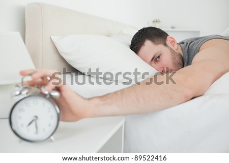 Attractive man being awakened by an alarm clock in his bedroom