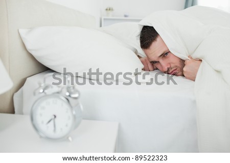 Annoyed man being awakened by an alarm clock in his bedroom