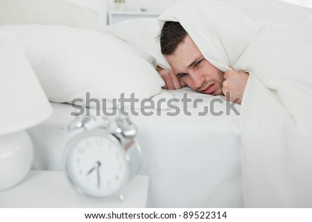 Man covering his ears while his alarm clock is ringing in his bedroom