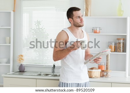 Good looking man drinking coffee while reading the news in his kitchen