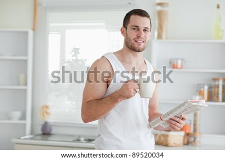 Delighted man drinking tea while reading the news in his kitchen