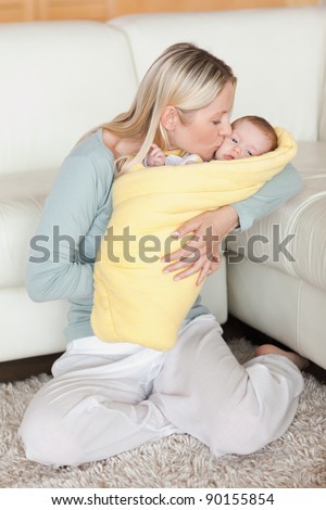 Young mom kissing her baby that is wrapped into a cover