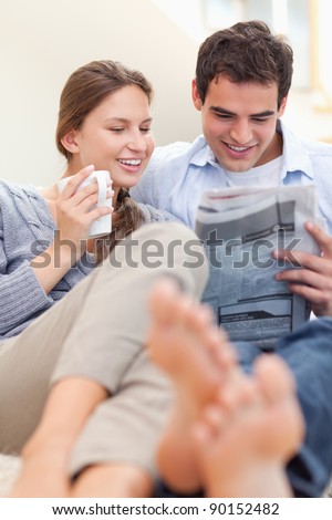 Portrait of a happy couple reading a newspaper in the morning in their living room