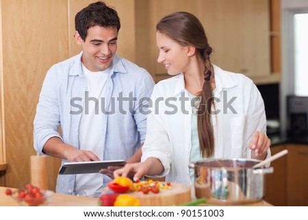 Charming couple using a tablet computer to cook in their kitchen
