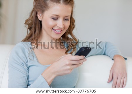 Young woman on the sofa reading text message on her smartphone