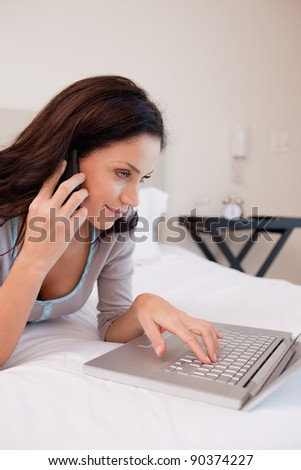 Side view of young woman on the bed with cellphone and laptop