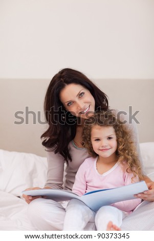 Young mother and daughter reading a book together on the bed