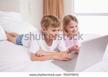 Smiling children using a notebook in a bedroom