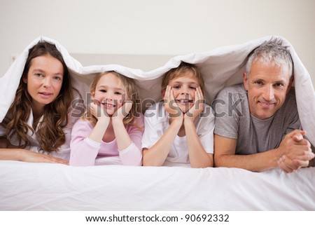 Family lying under a duvet in a bedroom