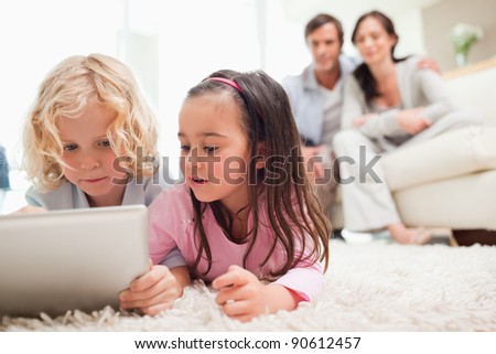 Cute siblings using a tablet computer while their parents are in the background in a living room