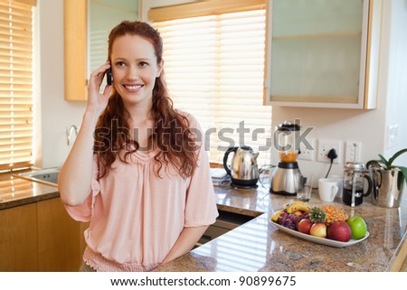 Woman with cellphone standing behind the kitchen counter