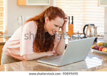 Woman in the kitchen looking confused at her laptop