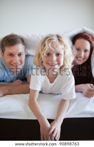 Cheerful boy under the bed cover together with his parents