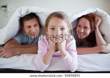 Cheerful girl under bed cover together with her parents