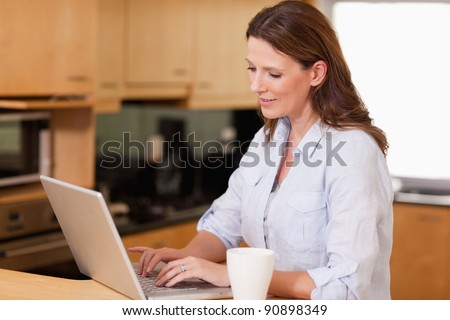Woman with cup in the kitchen using her laptop
