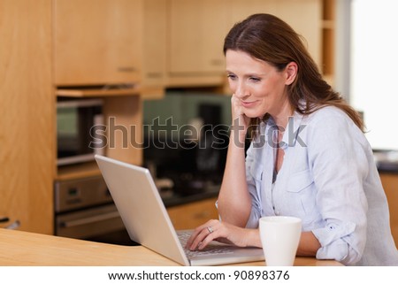 Smiling woman in the kitchen looking at her laptop