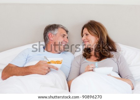 Happy mature couple eating cereals in bed