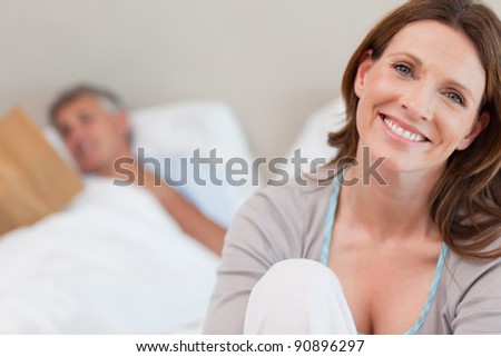 Smiling mature woman on the bed with reading husband behind her