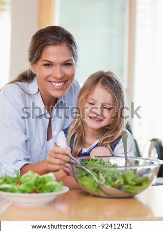 Portrait of a young mother and her daughter preparing a salad in their kitchen