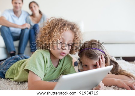 Young children using a tablet computer while their happy parents are watching in their living room