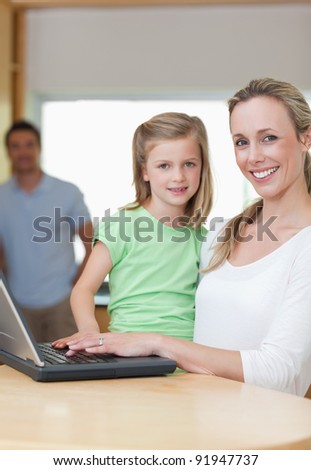 Mother and daughter using notebook together with father in the background
