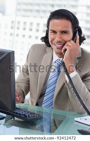 Portrait of a businessman working with a monitor while being on the telephone in his office
